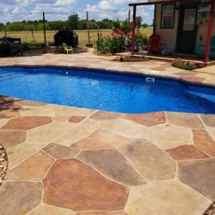 A large swimming pool with a stone patio in front of a house.