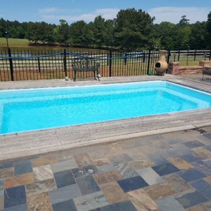 A large swimming pool is surrounded by a fence and a bench.