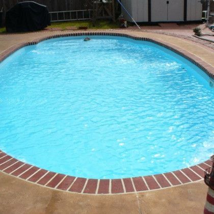 A large oval shaped swimming pool with a brick border