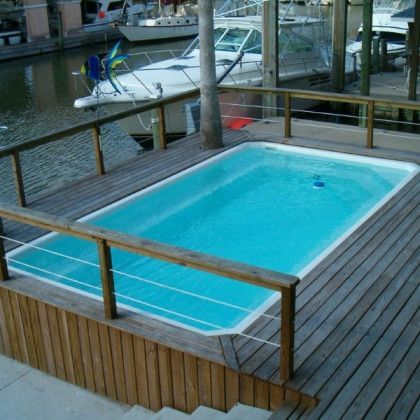 A swimming pool on a wooden deck with boats in the background