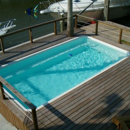 A swimming pool on a wooden deck with boats in the background