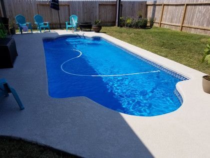 A large blue swimming pool in a backyard with chairs and a fence.