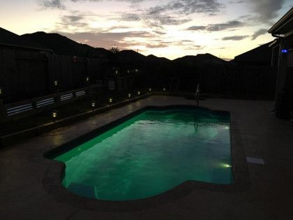 A swimming pool is lit up at night with mountains in the background.
