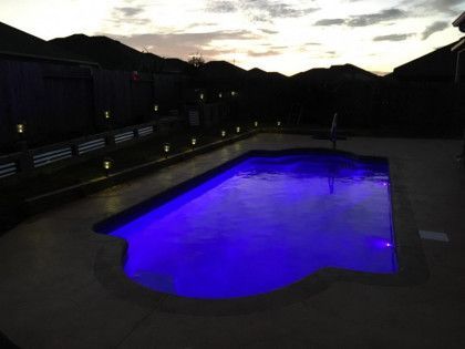 A large swimming pool is lit up with blue lights at night.