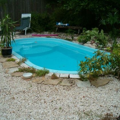 A small swimming pool surrounded by gravel and plants