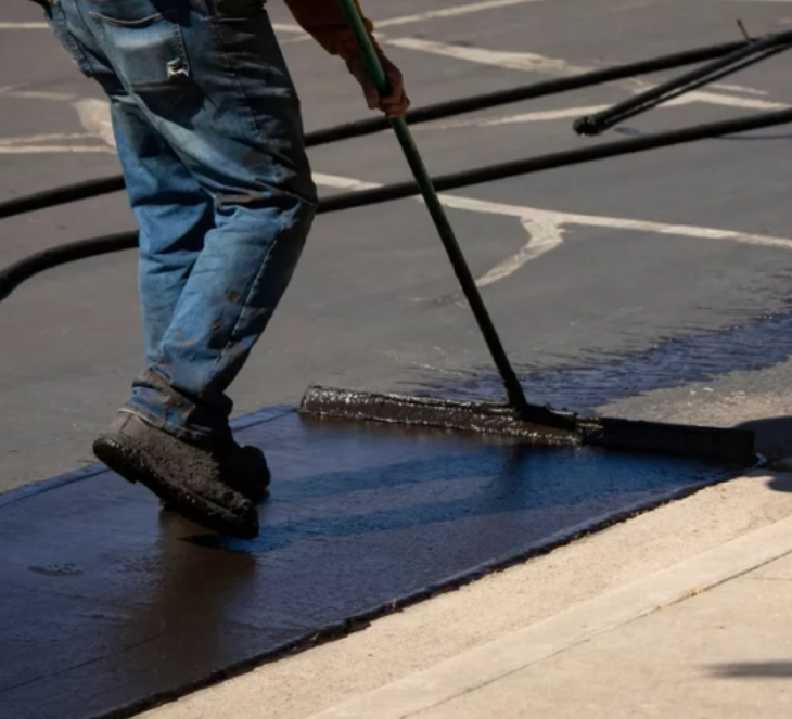 A man is using a broom to spread asphalt on a sidewalk