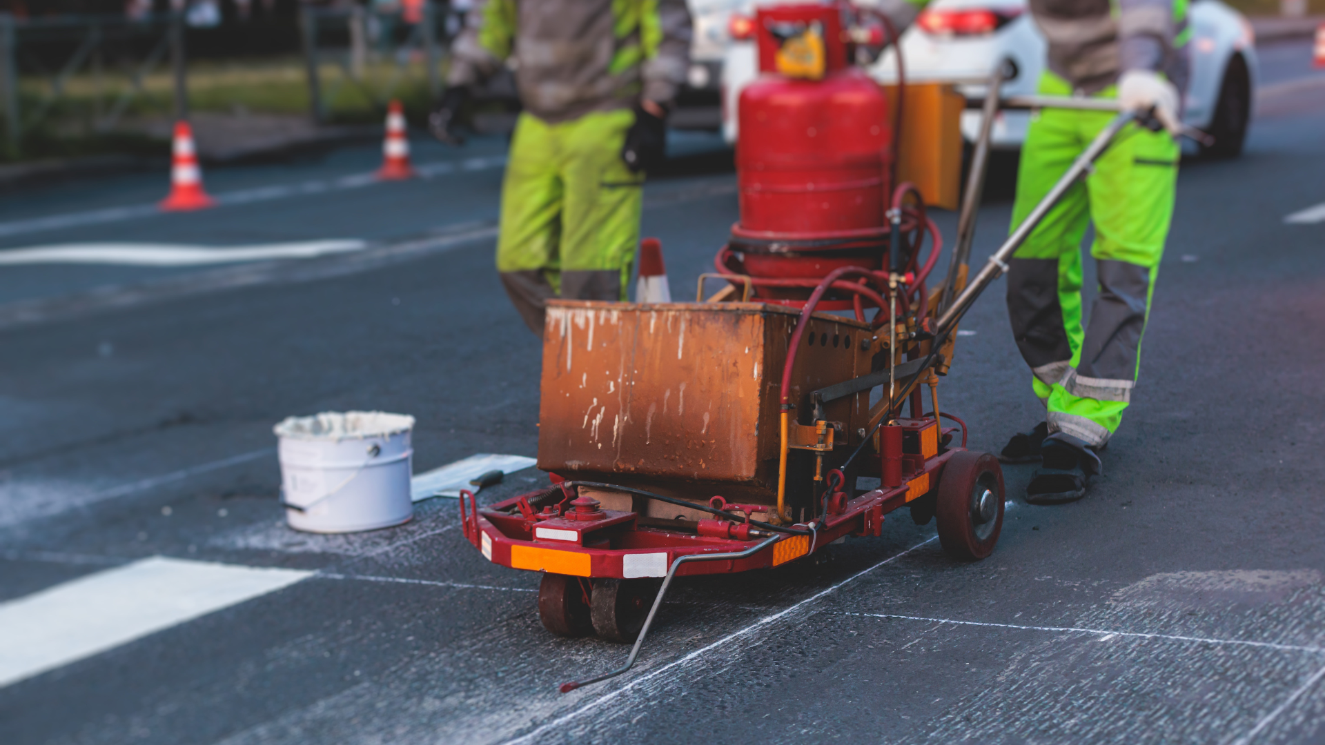 A man is using a machine to paint a crosswalk on a street.