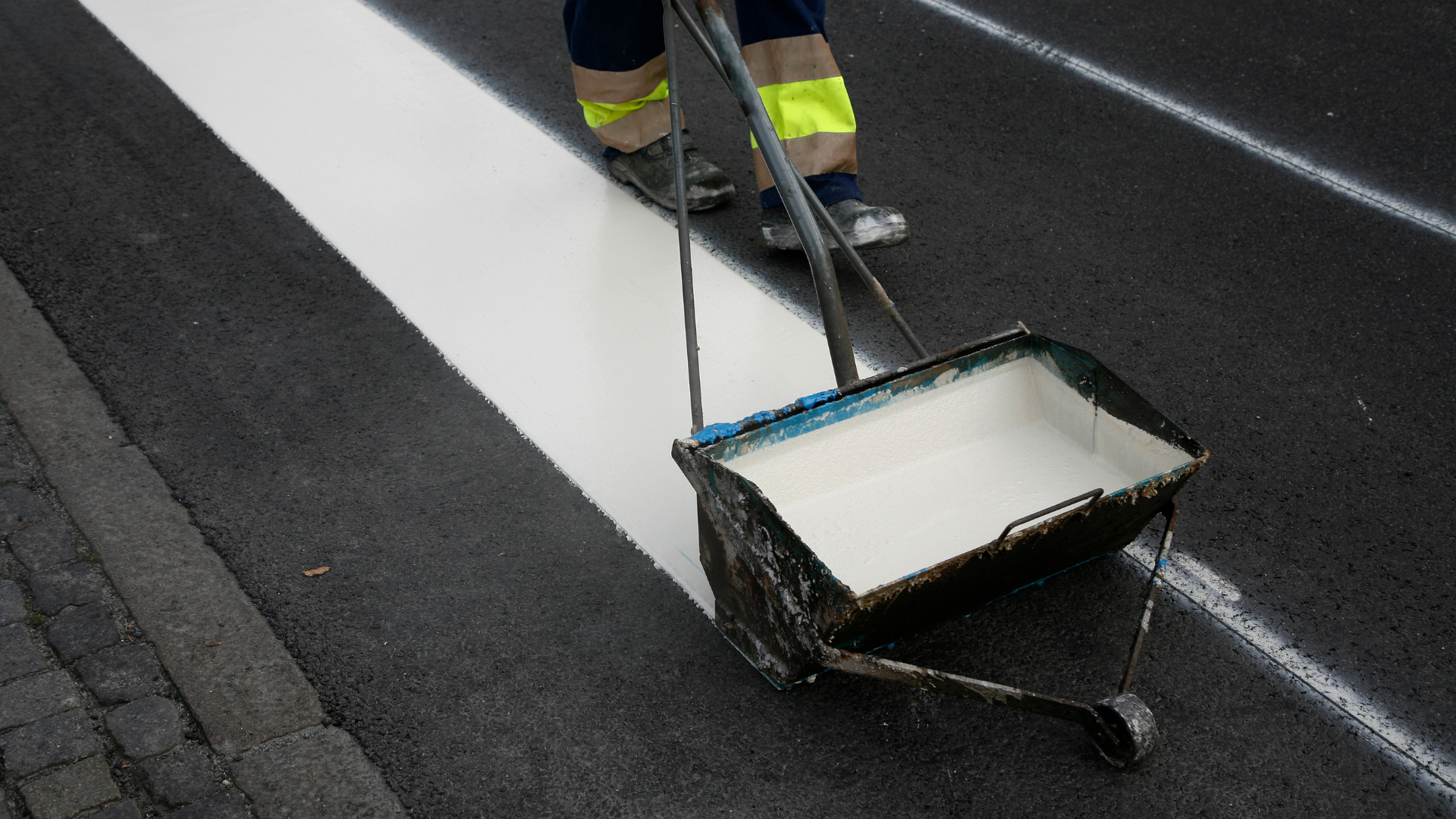 A person is painting a white line on the road with a roller.