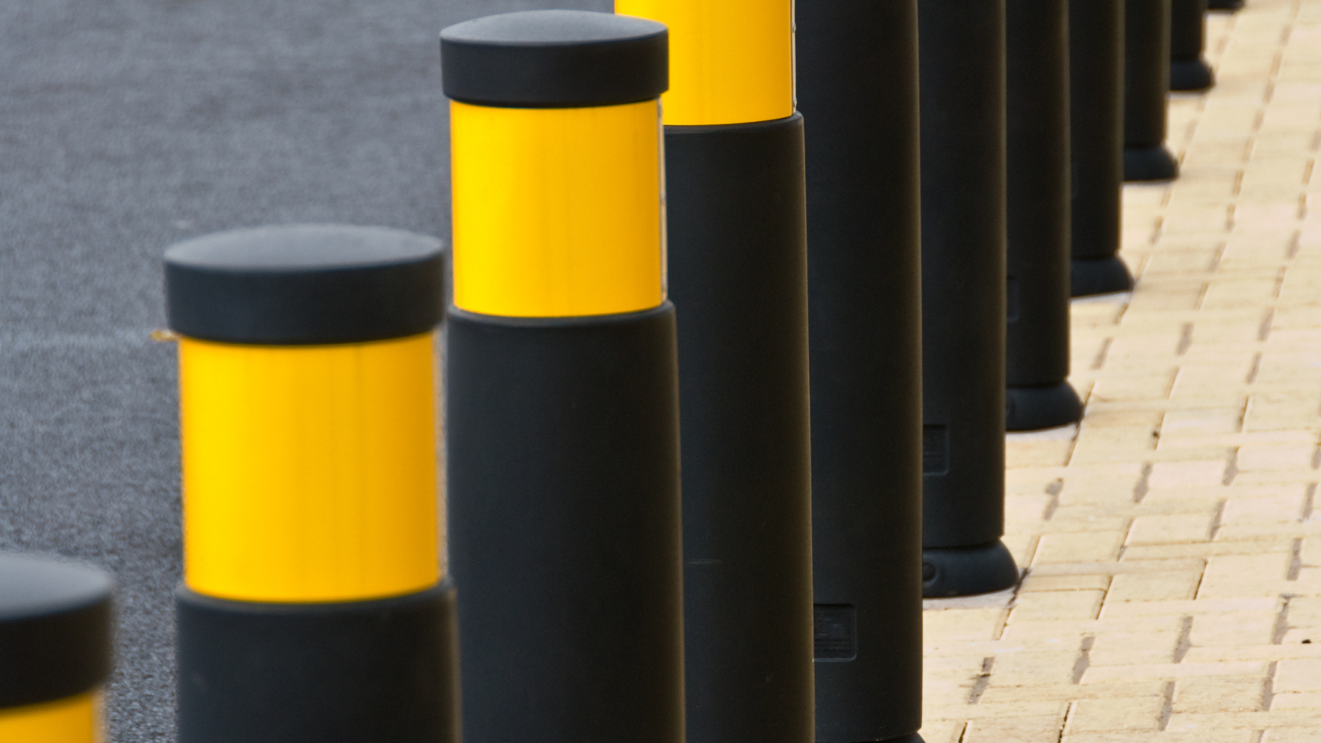 A row of yellow and black poles are lined up on a sidewalk.