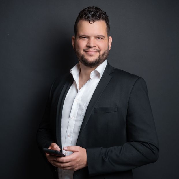 Ein Mann in Anzug und weißem Hemd hält ein Mobiltelefon.