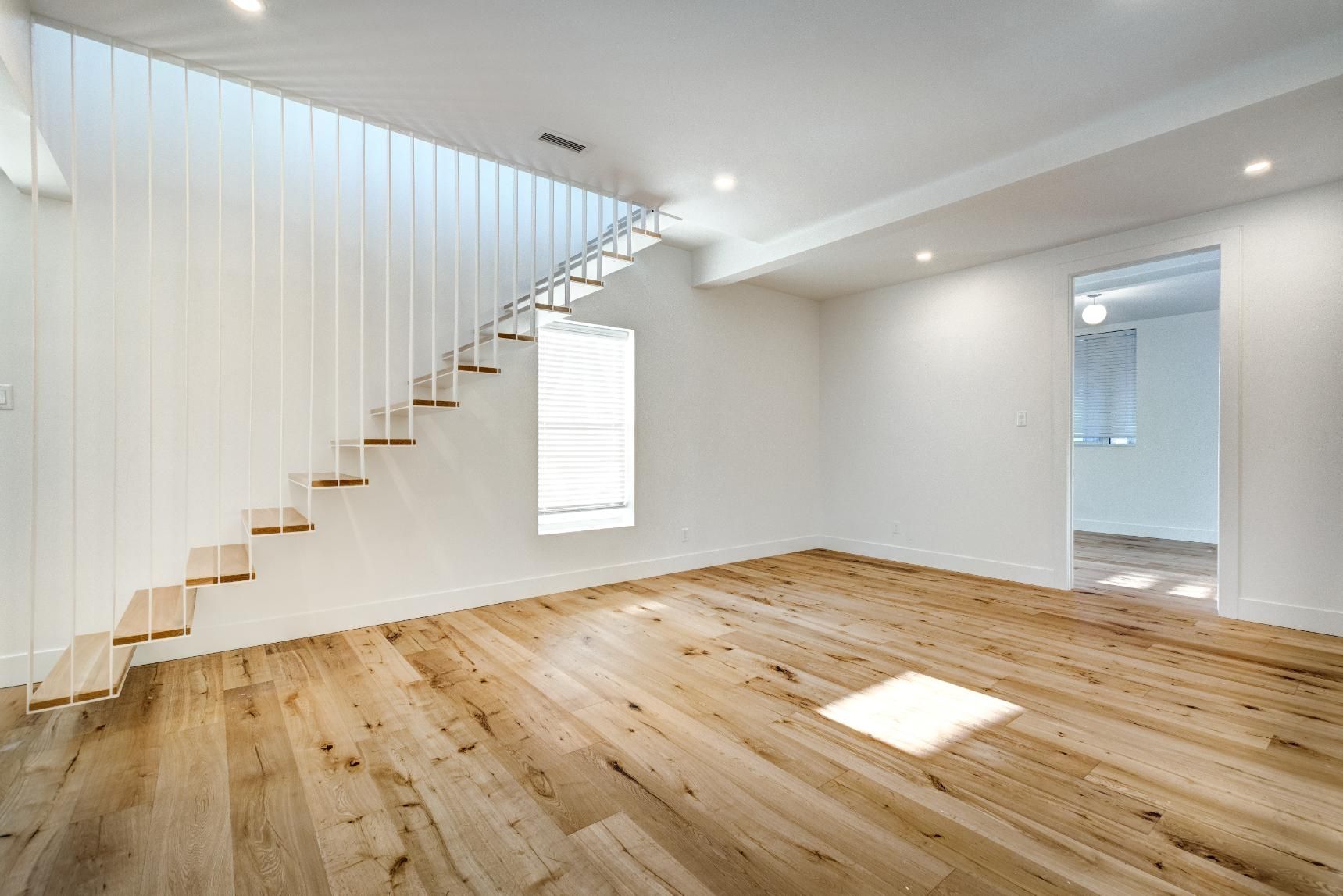 Bright modern empty room with wooden floor, white walls, floating staircase, and skylight window
