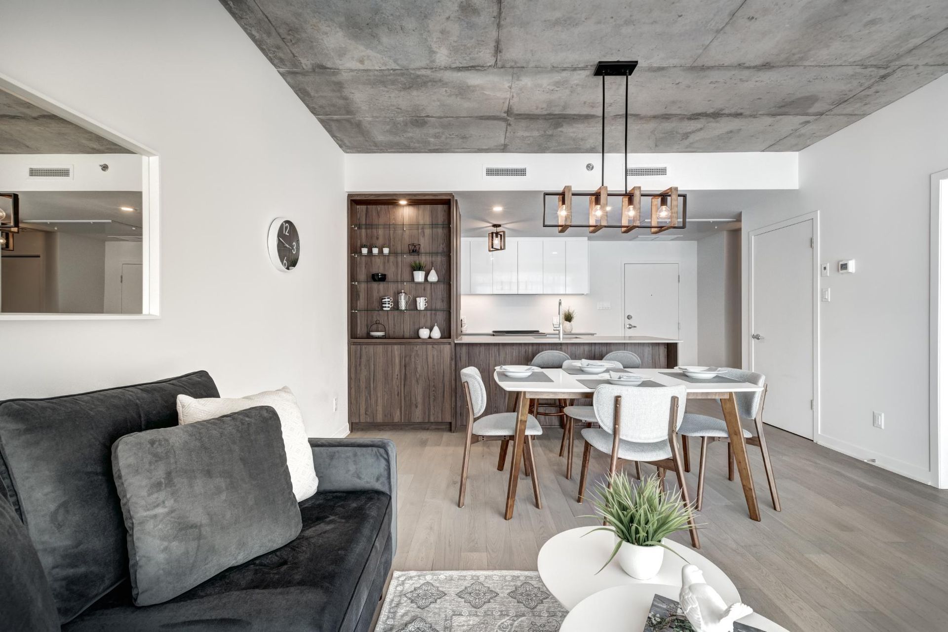 Modern open-concept living and dining room with gray sofa, white table, wood accents, and pendant lights