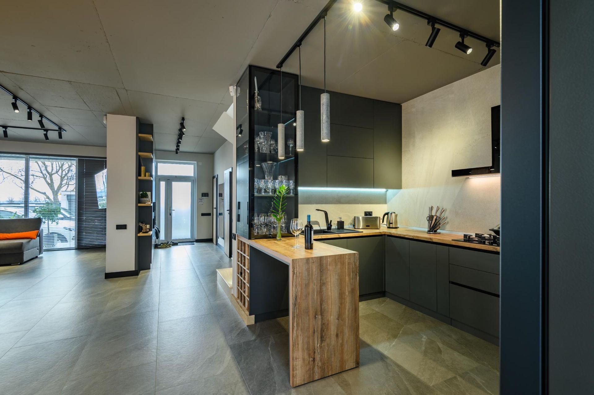 Modern open-plan kitchen with dark cabinets, wood island, and large windows.