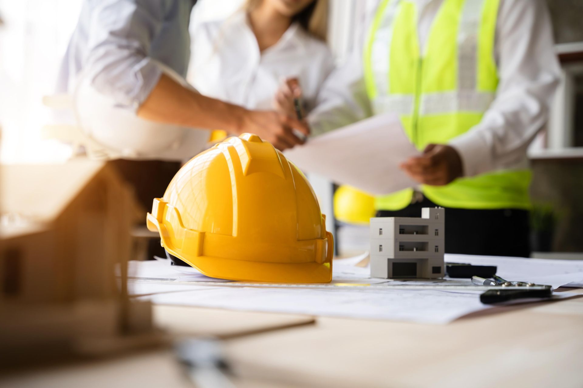 Construction workers reviewing plans beside a yellow hard hat and building model at a desk