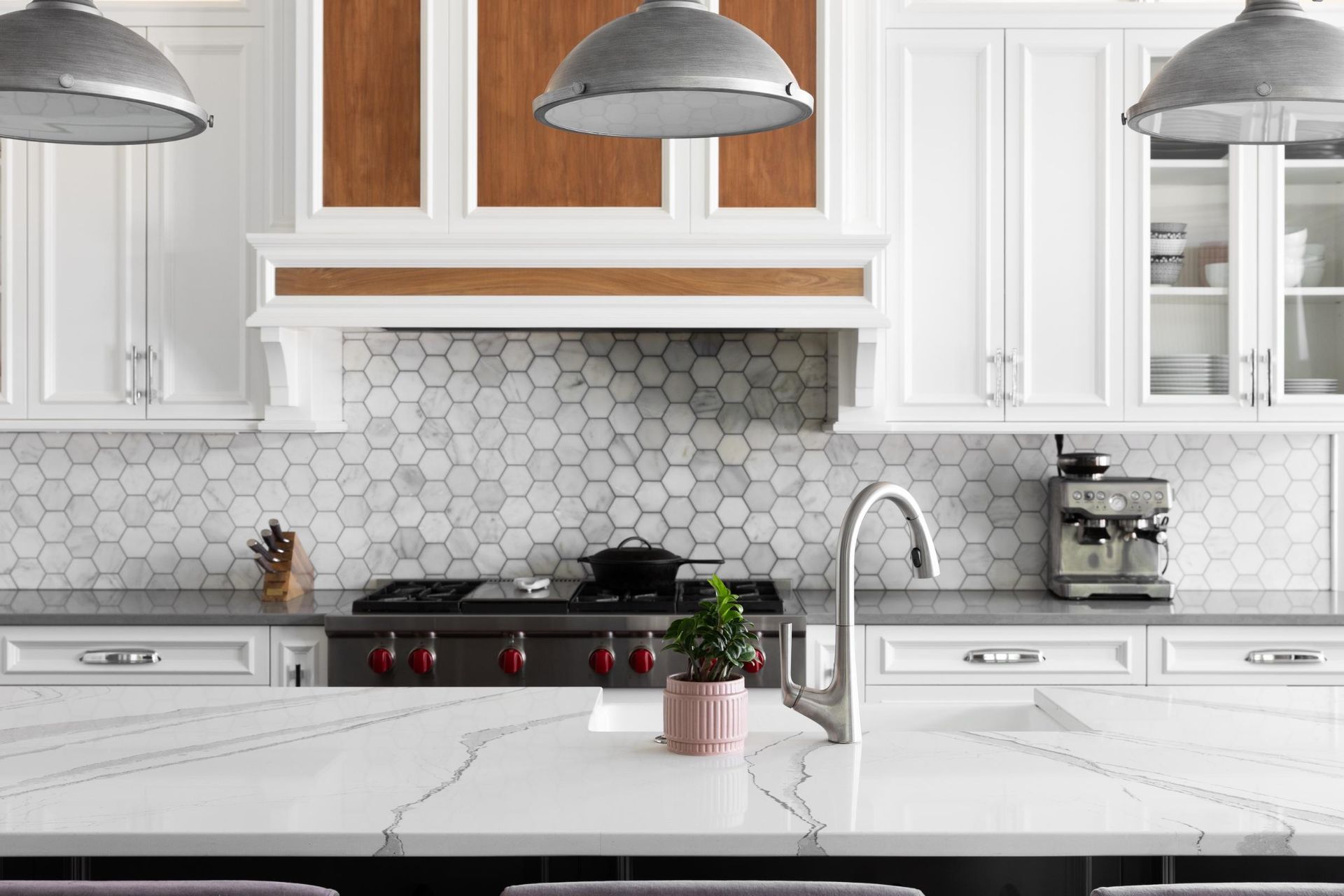 Bright modern white kitchen with hex tile backsplash, stainless stove, pendant lights, and marble island