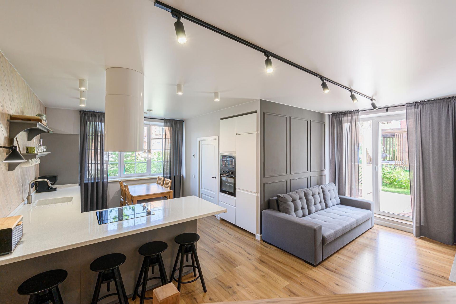Bright modern open-plan apartment with kitchen island, gray sofa, wood floors, and large windows.