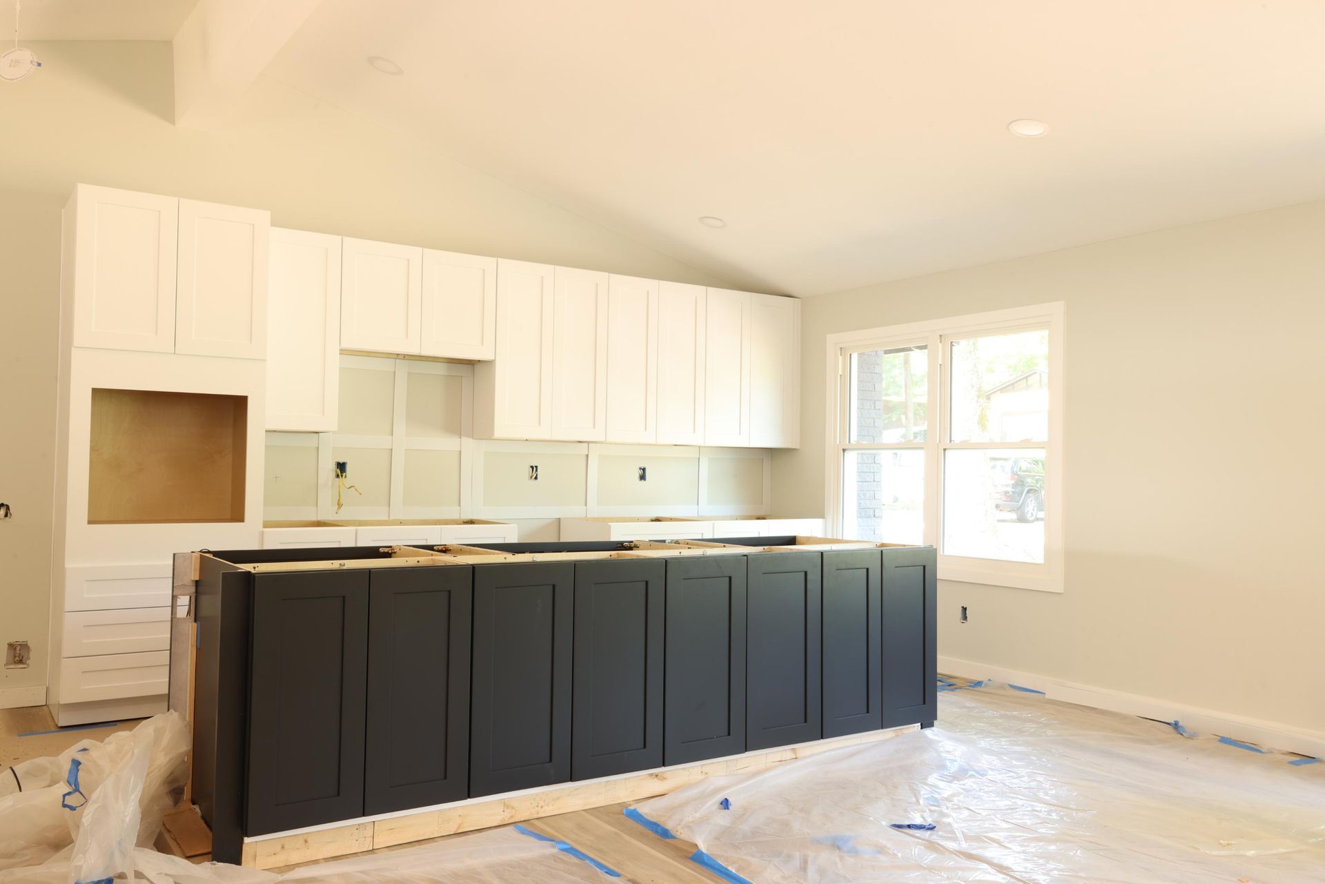 Kitchen under renovation with white cabinets and a dark island, protected by plastic floor covering