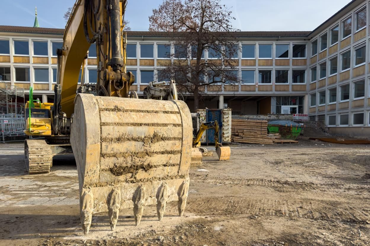 Excavator bucket in a muddy construction site in front of a large building