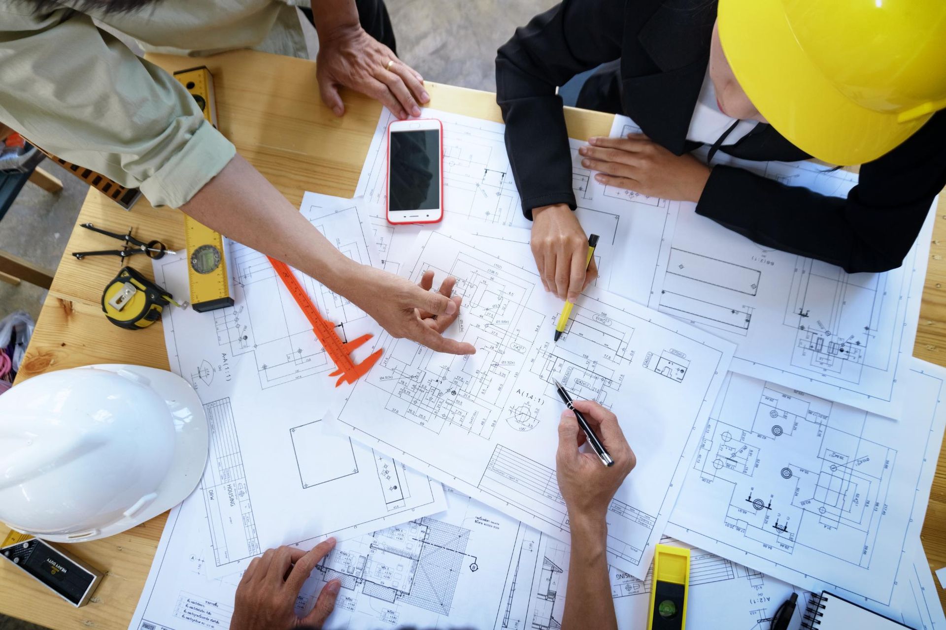 Engineers reviewing blueprints at a construction site with hard hats, tools, and a smartphone on the table
