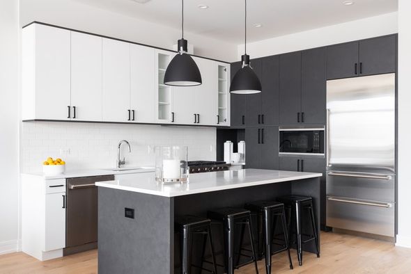 Modern kitchen with white and gray cabinets, island with black stools, stainless steel appliances, and pendant lights.