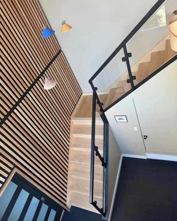 Wooden staircase in modern interior, black railing, slatted wood wall, overhead view.