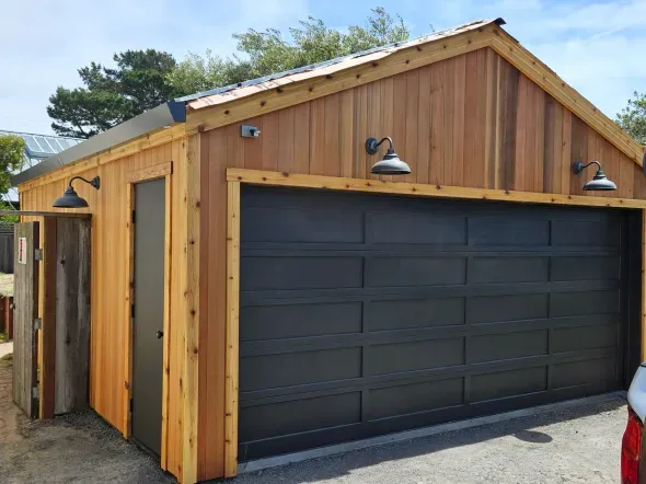 Cedar garage with black door and garage door, three black lights.