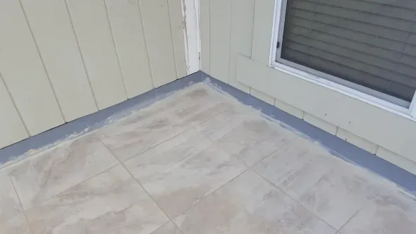 Tiled corner of a porch with gray trim and light yellow siding next to a window.