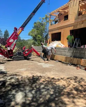 Construction workers using a crane to lift lumber at a building site. Sunny day.