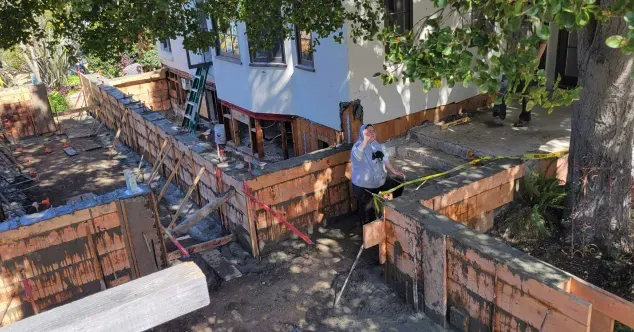 Construction site with a person standing by a retaining wall being built next to a house.