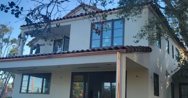 Two-story stucco house with a tiled roof, open windows, and a covered patio.