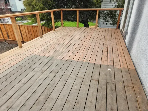 Wooden deck, partially cleaned, with a railing. The clean area is light brown; the dirty area is gray.