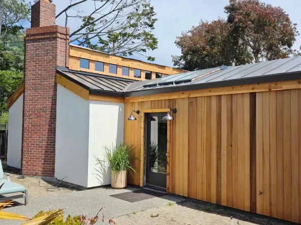 Modern home exterior with cedar siding, brick chimney, dark metal roof, and an entry door.