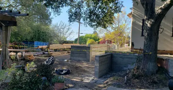 Construction site with concrete structures, trees, and a building on a sunny day.