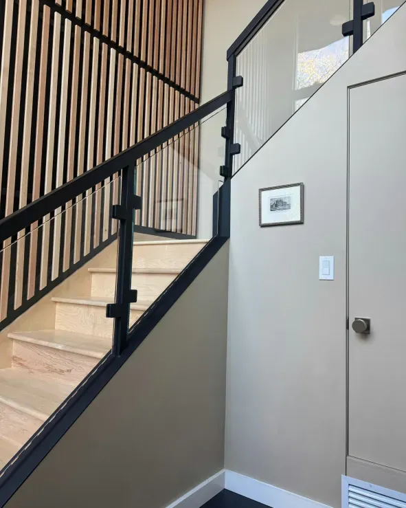 Staircase with wood and glass railing, beige walls, and a small framed picture.