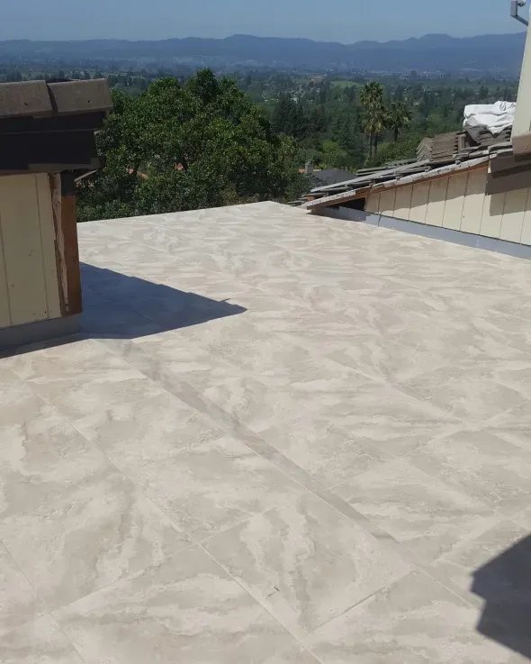 Flat rooftop with light-colored, patterned surface, view of distant hills and trees.