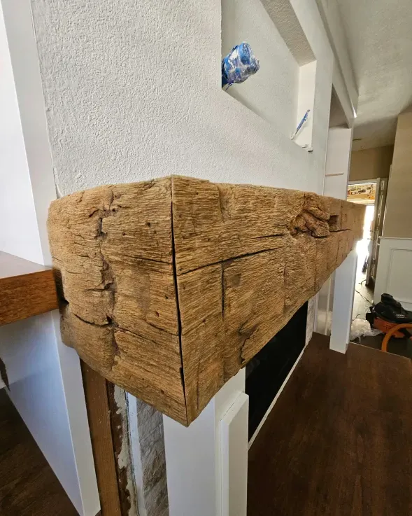 Wooden mantelpiece corner over a fireplace, with textured brown wood and white surrounding trim.
