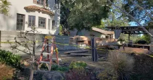 Construction site next to a stucco building with a red ladder and wood materials.