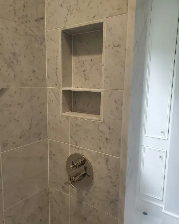 Marble-tiled shower with built-in storage niches and chrome shower controls.