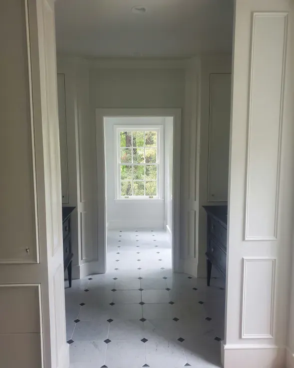 Hallway with white walls, black and white tiled floor, and a window at the end.