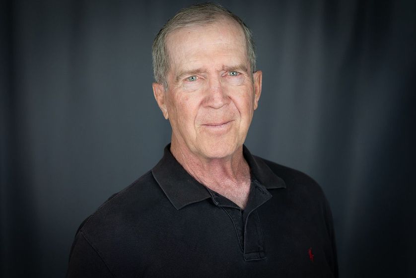 Man in black polo shirt smiles, looking slightly to the side against a dark gray backdrop.
