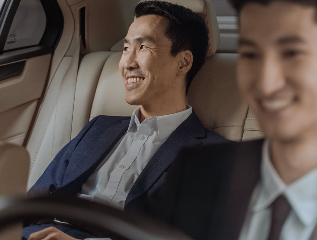 Two men in business attire smiling in a car, one in the back seat and one in the foreground