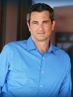 A man in a suit and white shirt is smiling for the camera.
