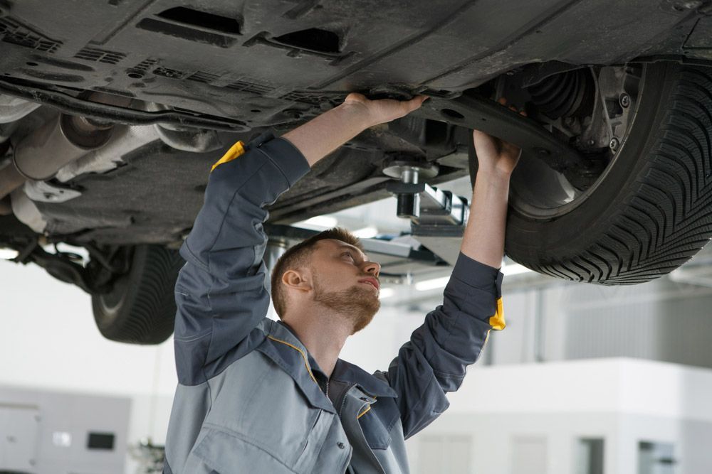 Mechanic Inspecting Underside of Car on a Lift in a Workshop — Carline Automotive Solutions in Bungalow, QLD