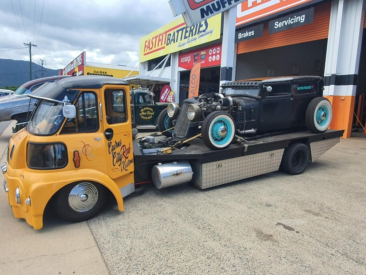 A Yellow Tow Truck with A Black Car on The Back Is Parked in Front of Garage — Carline Automotive Solutions in Bungalow, QLD