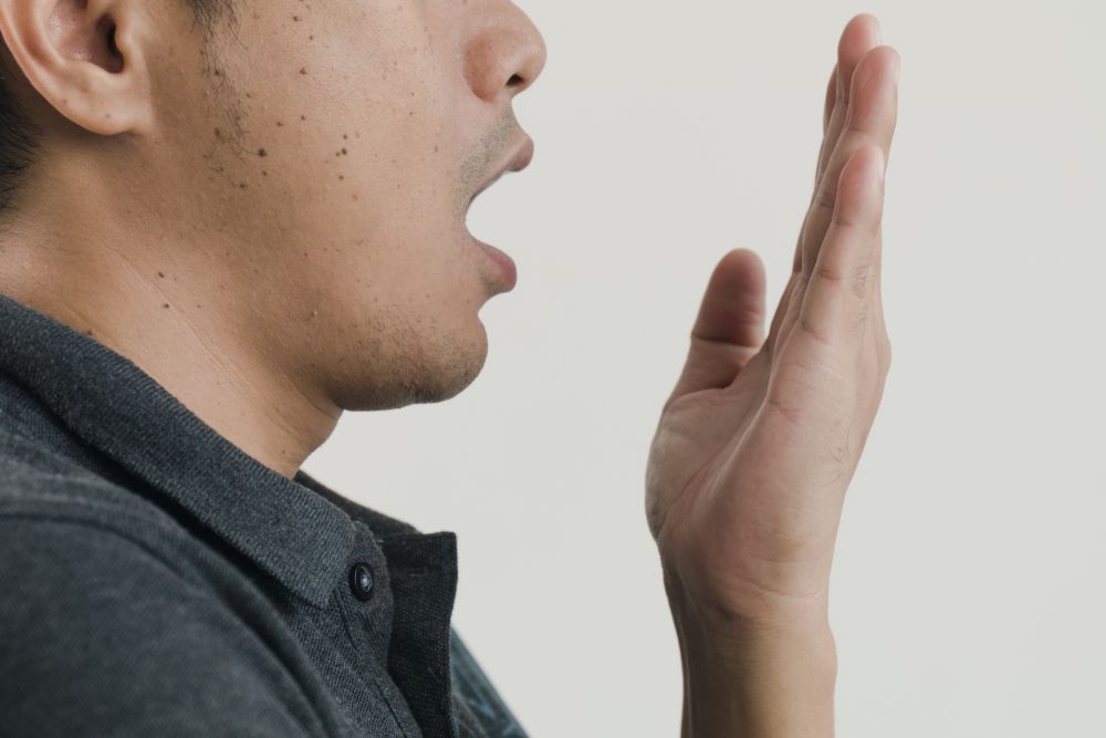 Man exhales toward his hand, checking for bad breath.