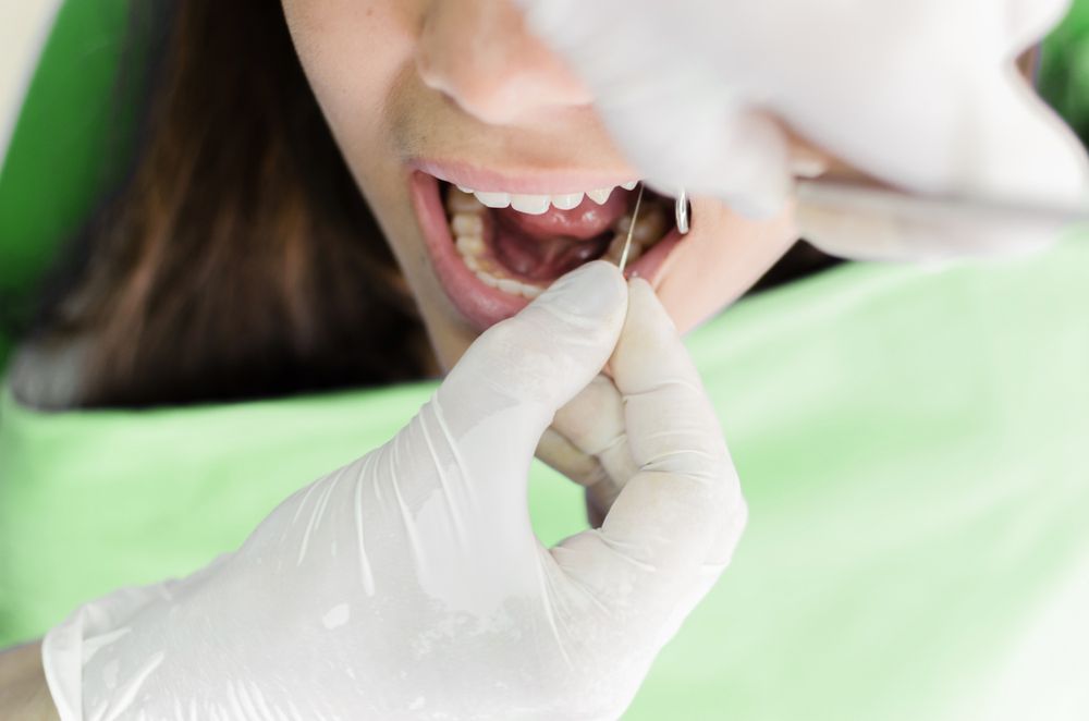 Dentist examining patient's teeth with dental tools; indoors.