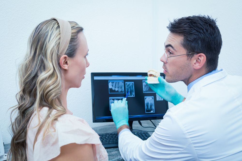 Dentist showing x-rays to a patient, holding a model tooth in office.