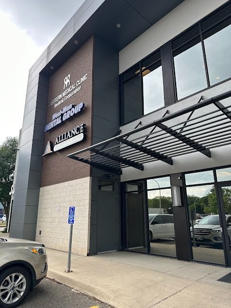 Exterior view of a medical clinic with signage, including the name and logo. A parking spot has an accessibility sign.