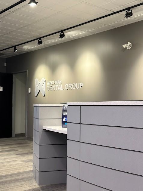 Reception area with dental group logo above reception desk, gray and white tones.