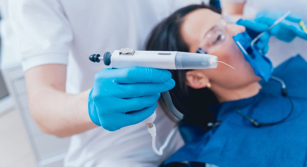 Dentist using a dental tool on a patient. Blue gloves, patient's mouth isolated, white setting.